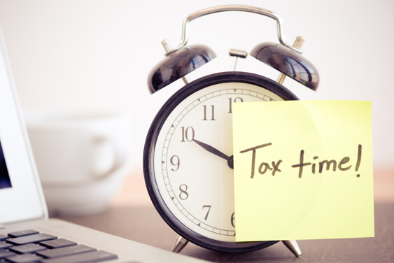 A clock with tax time post it note on it.