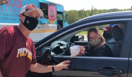 A masked IC System employee posing while giving another IC System employee food at the drive thru event