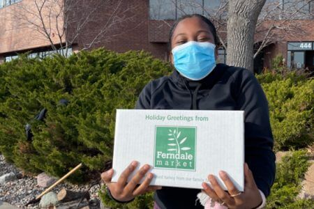 A masked IC System employer holding a thanksgiving turkey in a box gifted by IC System