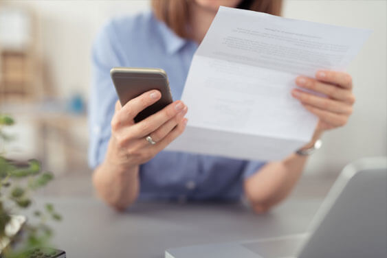 A woman is reading a letter and holding her phone